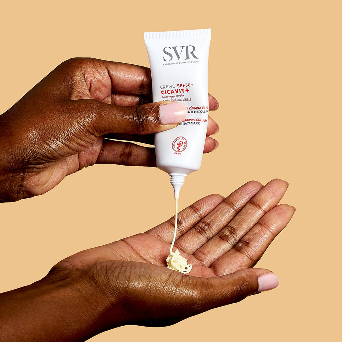 SVR CICAVIT+ SPF50+ cream being squeezed from a white tube onto a palm against a tan background.