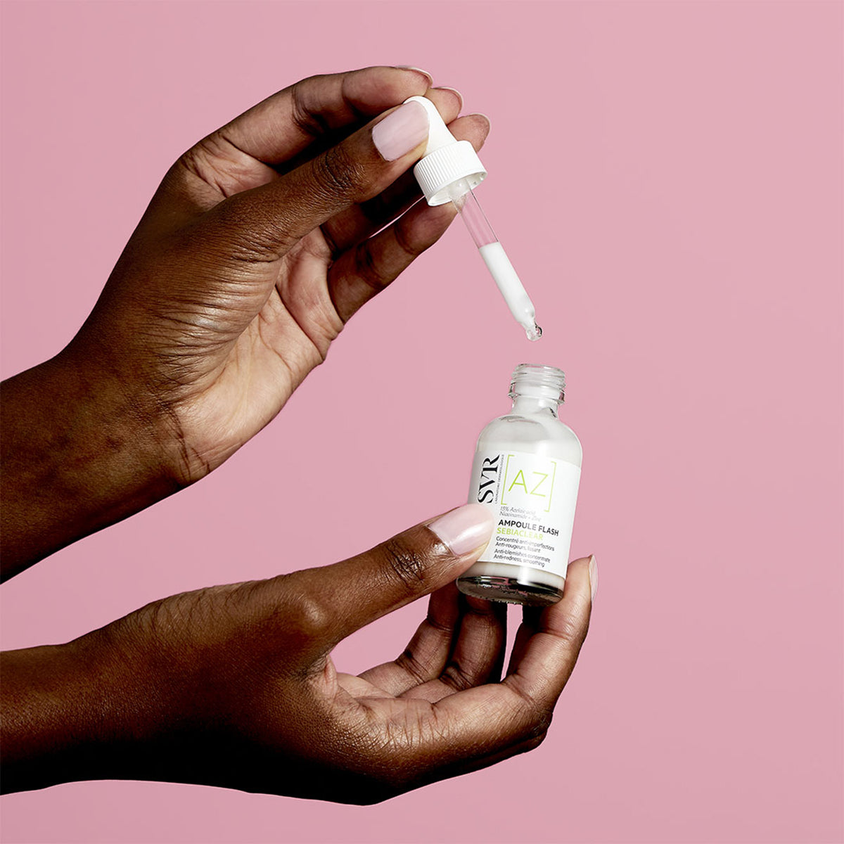 Hands holding a SVR Sebiaclear Ampoule Flash bottle with a white dropper against a solid pink background.