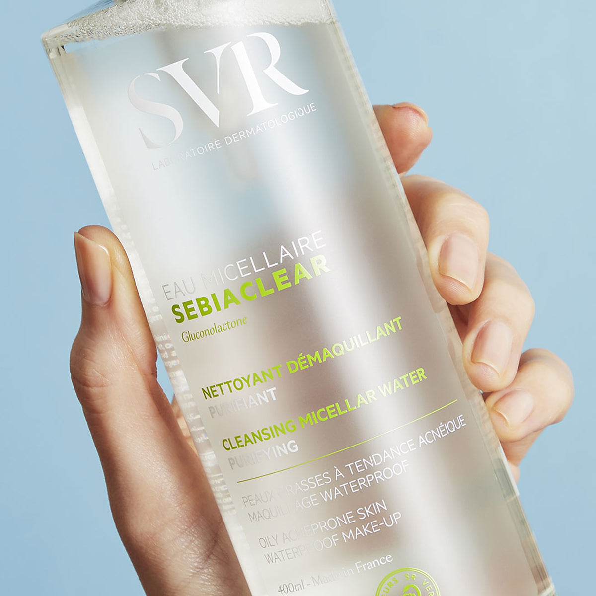 Hand holding a clear 400ml bottle of SVR Sebiaclear purifying micellar water against a light blue background.