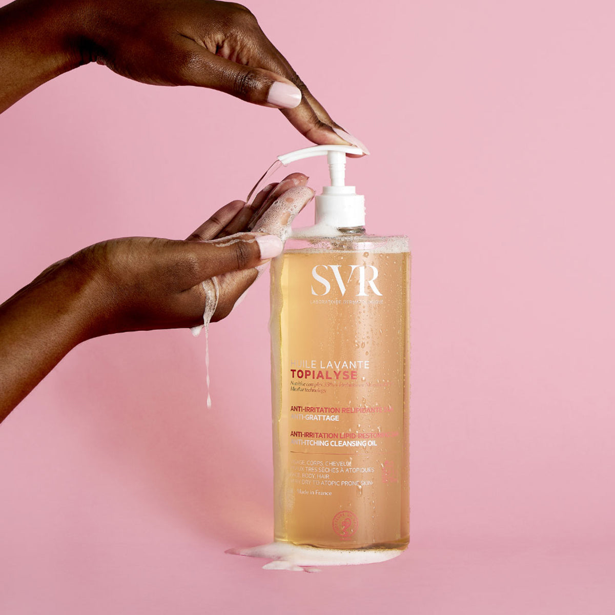 SVR TOPIALYSE Huile Lavante cleansing oil bottle with pump dispenser being used by hands against a pink background.