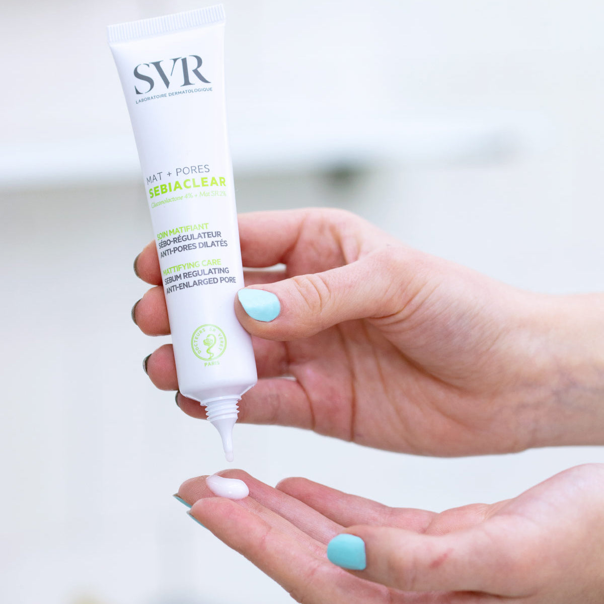SVR Sebiaclear Mat+Pores white squeeze tube dispensing a small amount of mattifying cream onto a hand.
