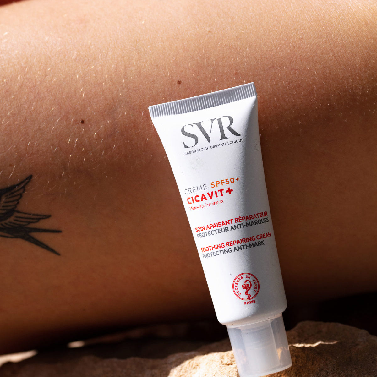 White SVR CICAVIT+ SPF50+ soothing repairing cream tube resting on a rock against a sunlit arm.