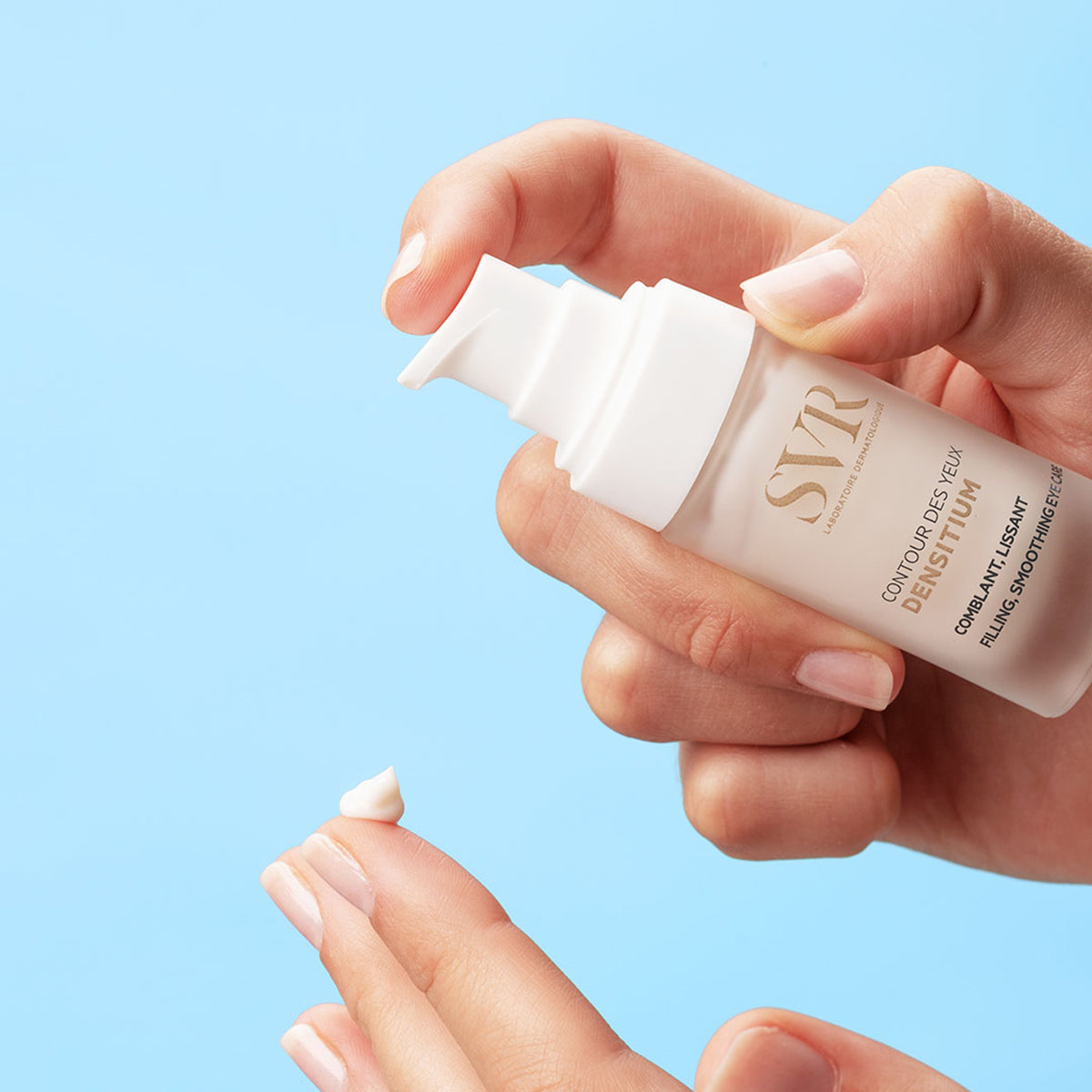 Hand dispensing white SVR Densitium eye cream from a sleek, frosted pump bottle against a light blue background.