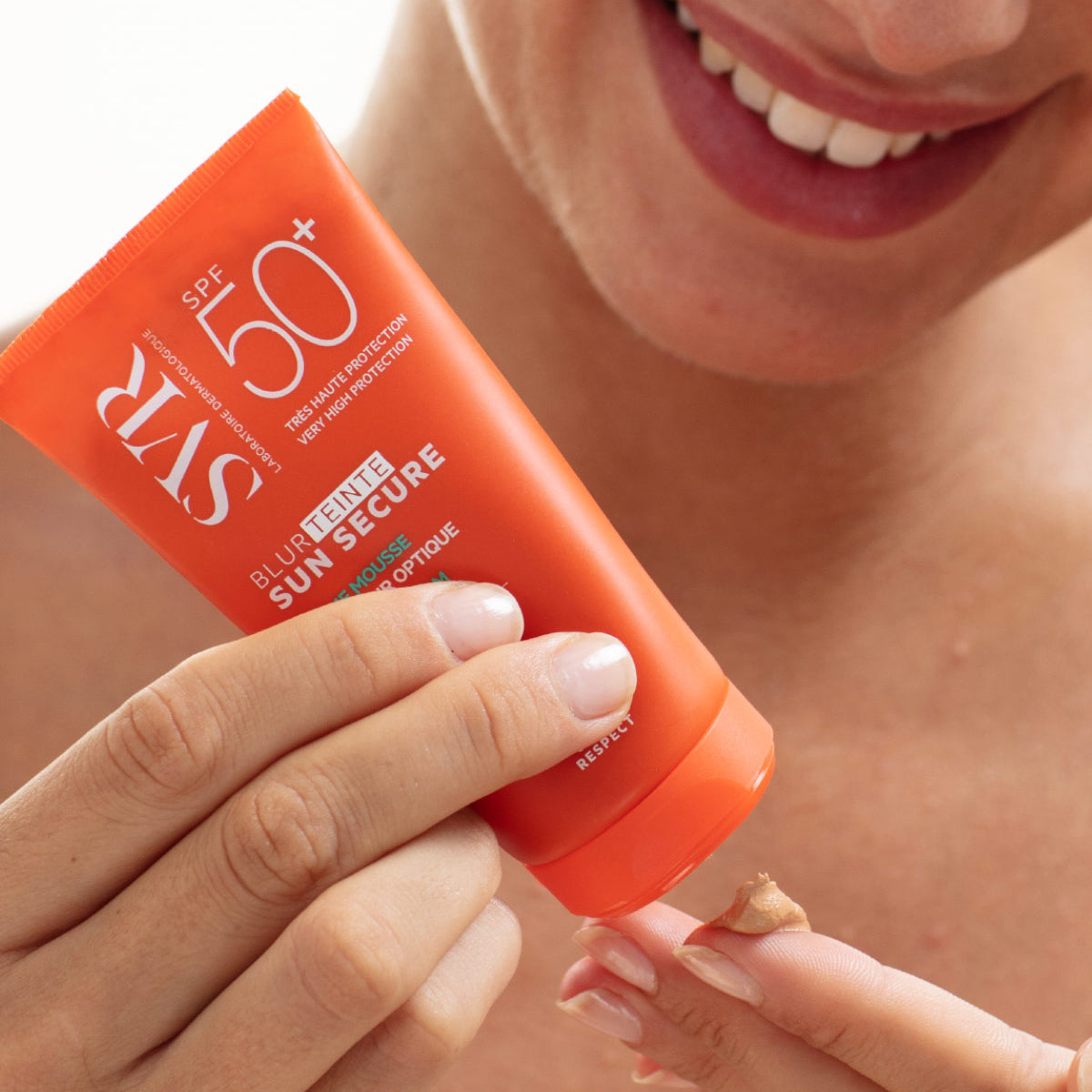 Woman squeezing a beige mousse from an orange SVR SUN SECURE Blur Teinte SPF50 tube onto her fingertip.