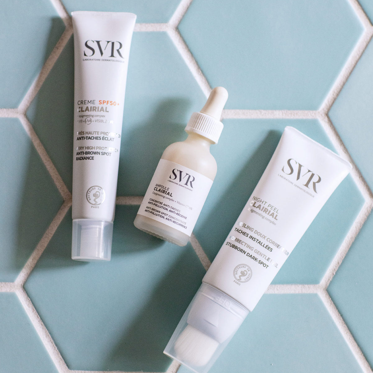 SVR Clairial skincare set with two white tubes and a dropper bottle on a blue hexagonal tiled surface.