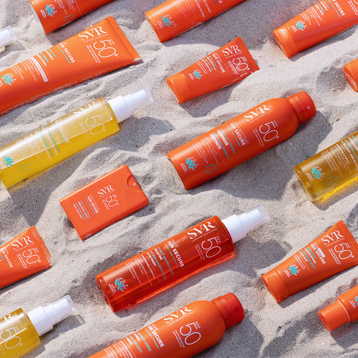 Assorted SVR SUN SECURE SPF50+ sunscreen tubes and spray bottles arranged on textured beach sand.