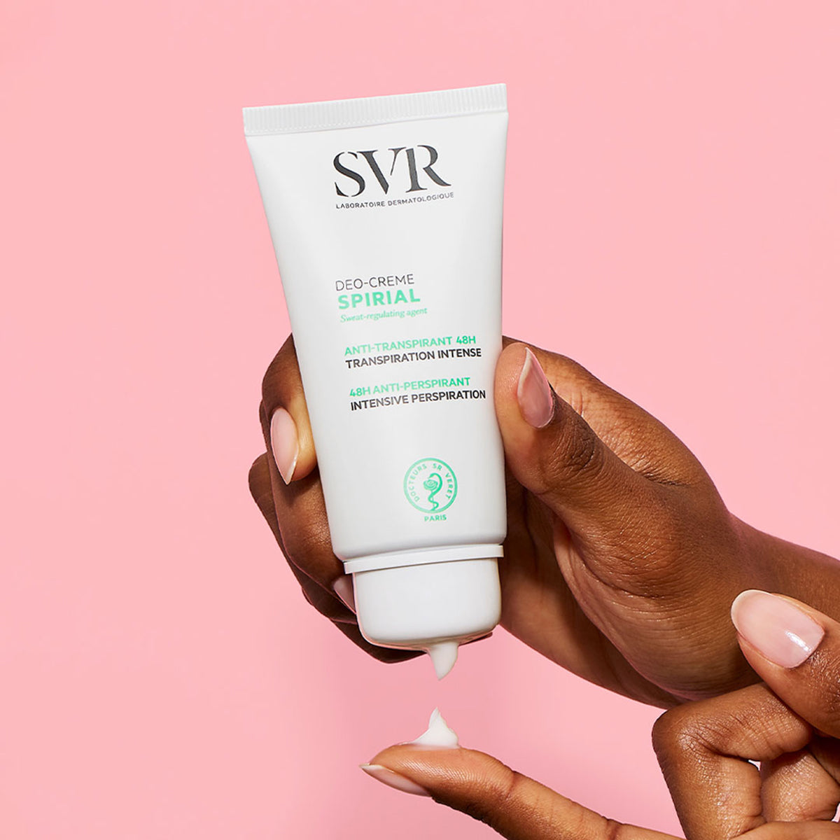 SVR Spirial Deo-Creme white squeeze tube held in hand, dispensing white cream onto a finger against a pink background.