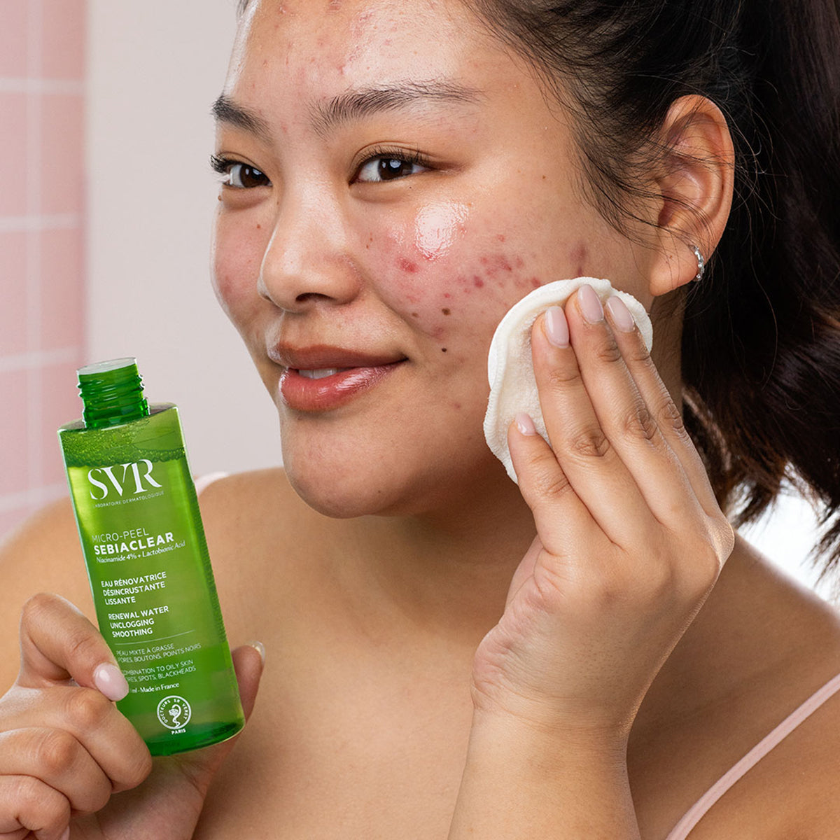 Woman applying SVR Sebiaclear Micro-Peel renewal water with a cotton pad to her face to treat acne and blemishes.