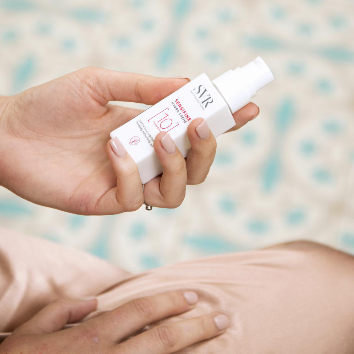 White pump bottle of SVR Sensifine Hydra-Creme held in a hand against a soft, light-colored background.