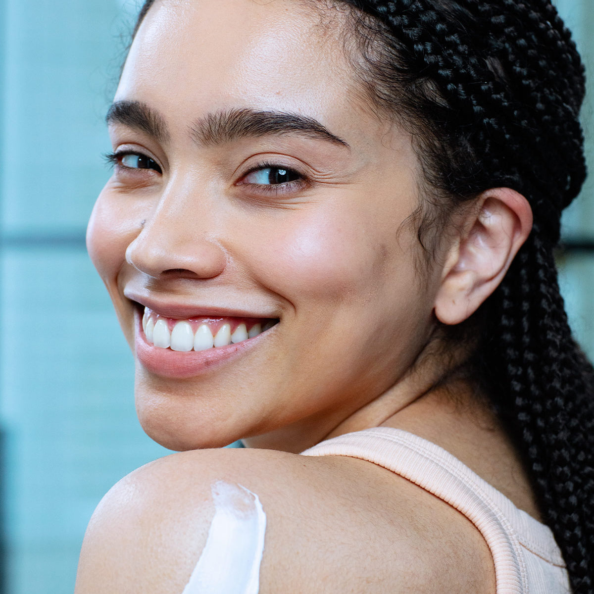 Smiling woman with braided hair applying white XERIAL 10 Lait moisturizing cream to her shoulder.