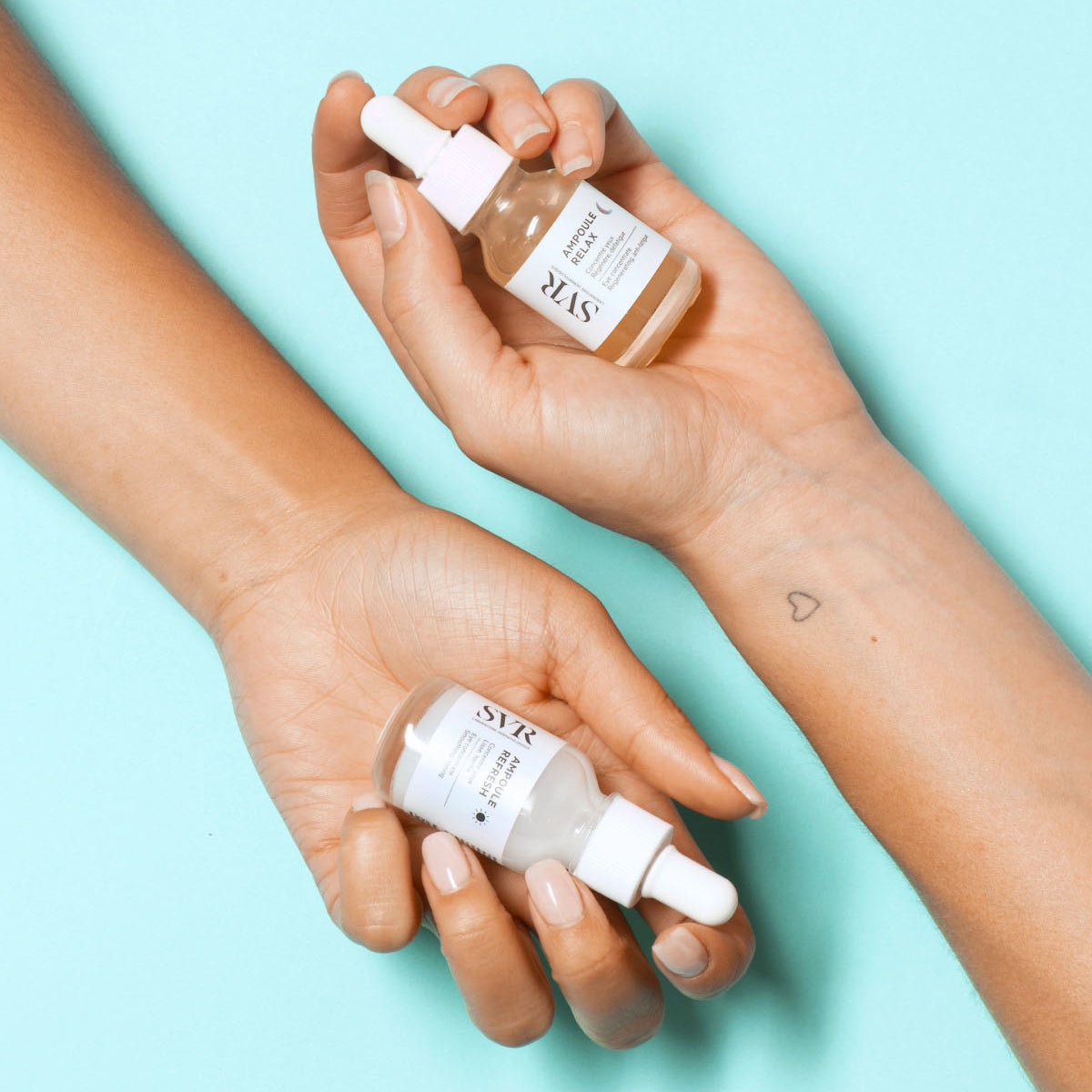 Two hands holding SVR Ampoule Refresh and Relax glass dropper bottles against a light blue background.
