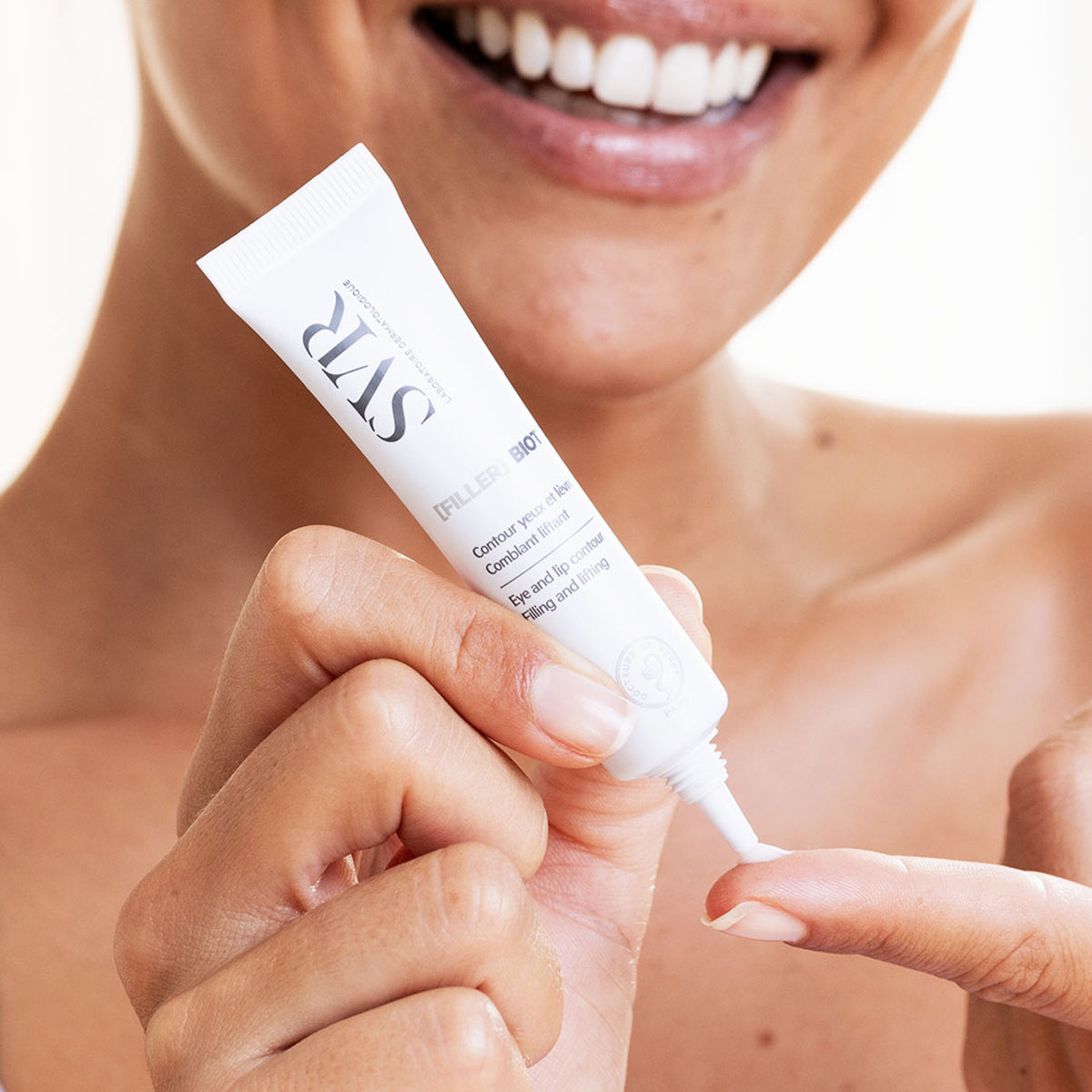 White SVR [FILLER] Biotic eye and lip contour cream tube being applied to a finger by a smiling woman.
