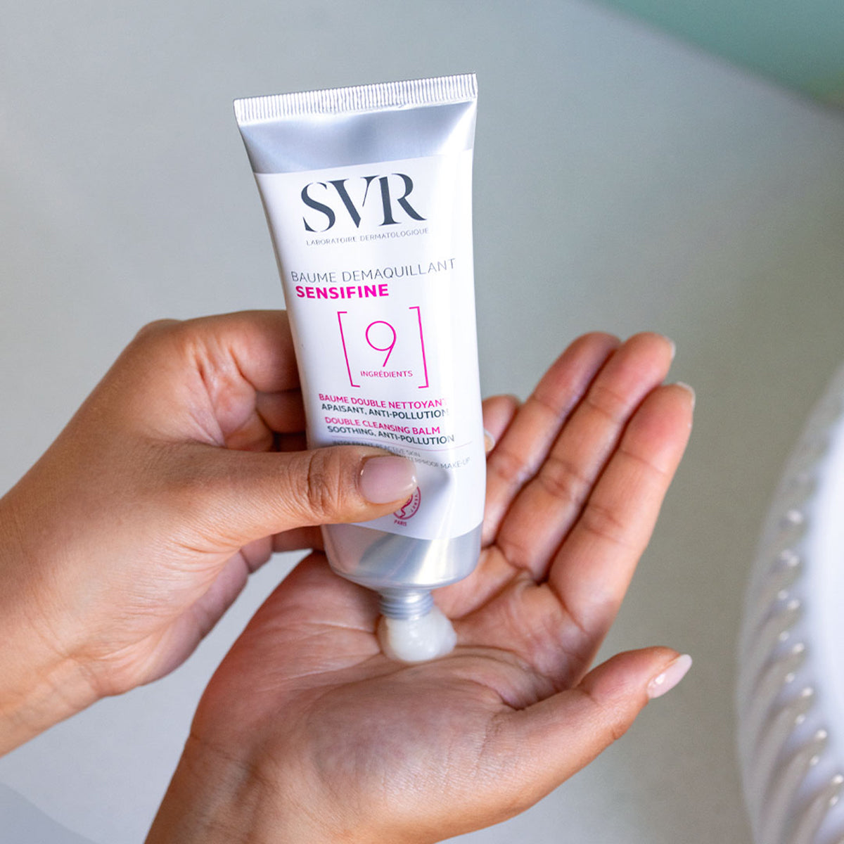 SVR Sensifine Baume Demaquillant cleansing balm being squeezed from a silver tube into a hand.