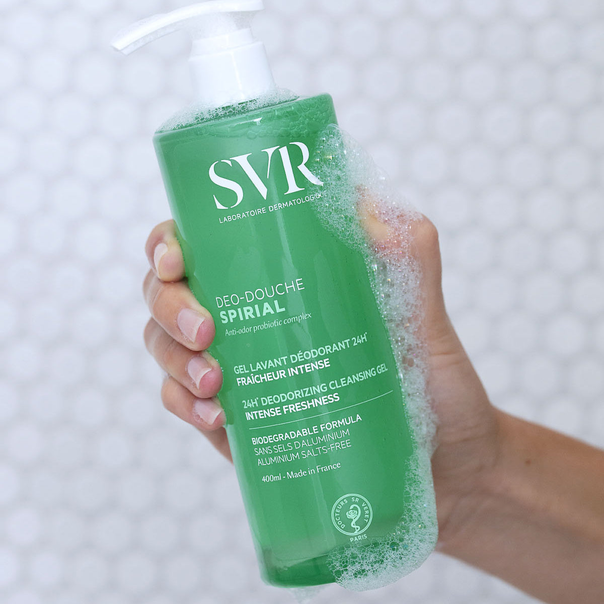 Hand holding a 400ml green bottle of SVR Spirial Deo Douche cleansing gel with white pump and soapy lather.