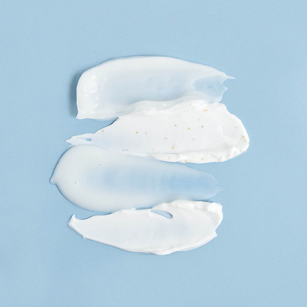 Three smooth white cream swatches with golden particles on a light blue background.