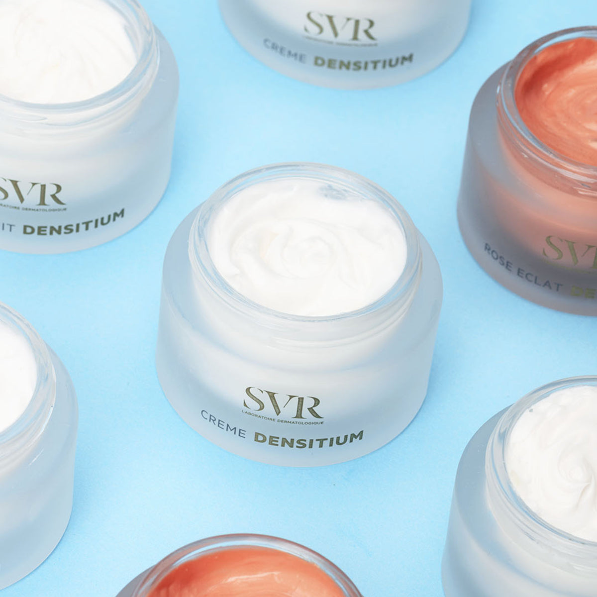 Open jars of SVR Densitium face cream with white and rose-tinted textures in frosted glass containers on a blue background.