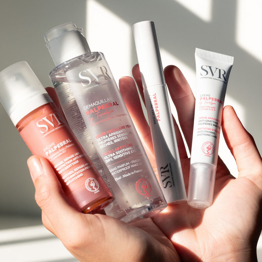 Hand holding four SVR Palpebral skincare products including a pink balm, clear micellar gel, mascara, and soothing eye cream.