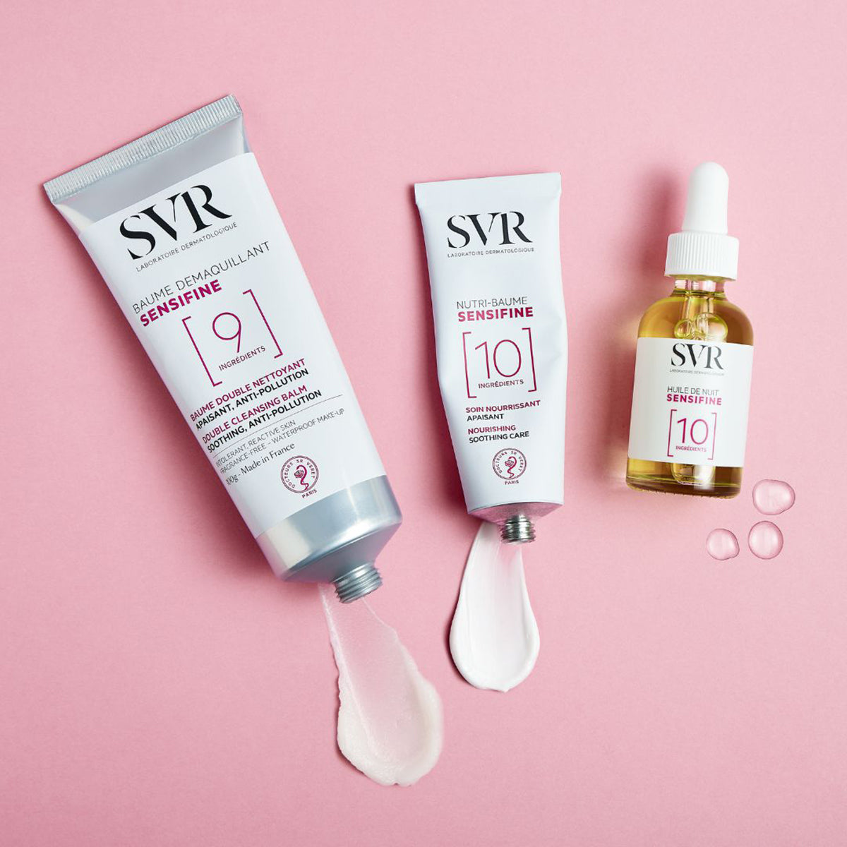 SVR Sensifine skincare set featuring two white tubes and a glass dropper bottle with serum on a pink background.