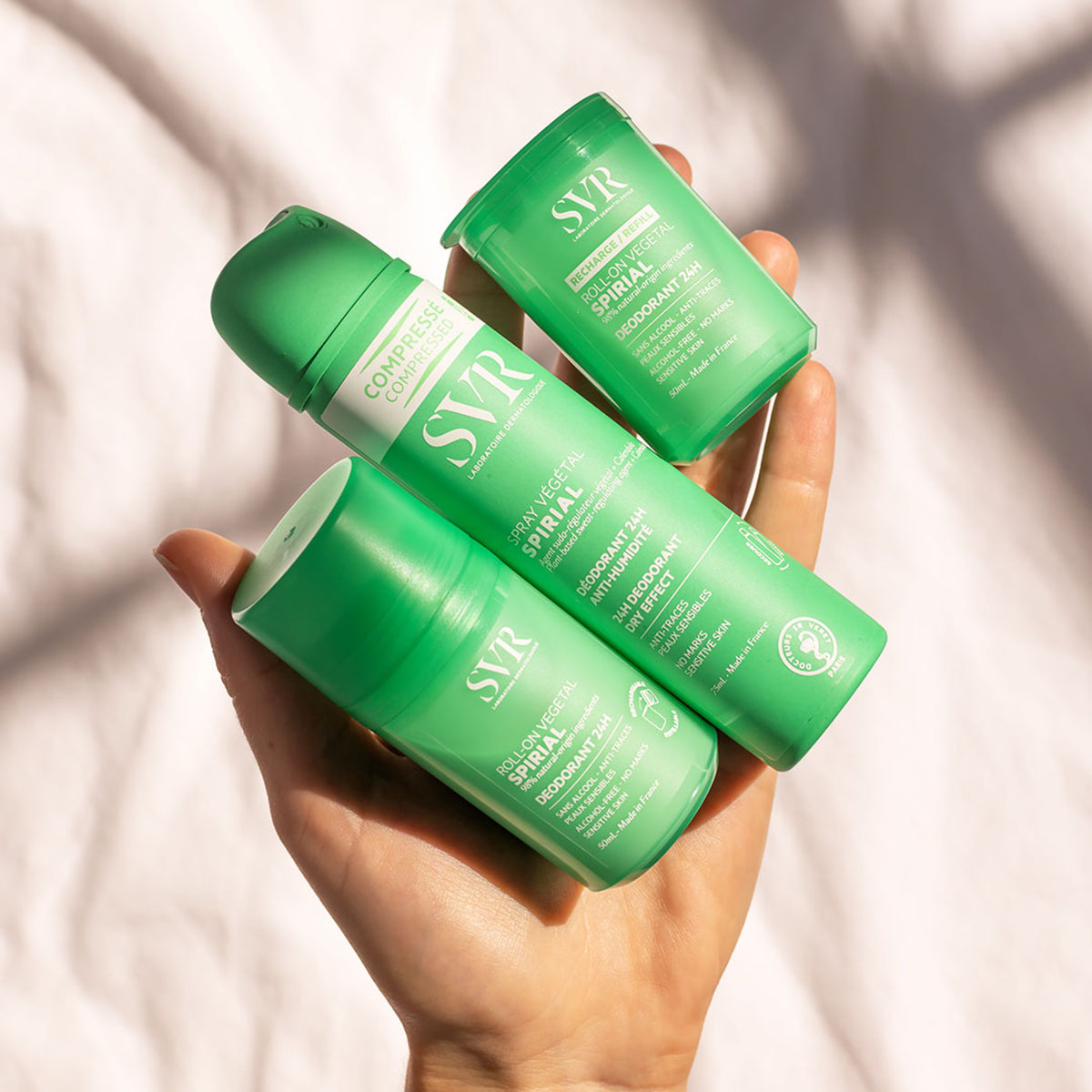 Hand holding three green SVR Spirial Vegetal deodorant bottles, including a spray and two roll-on refills.