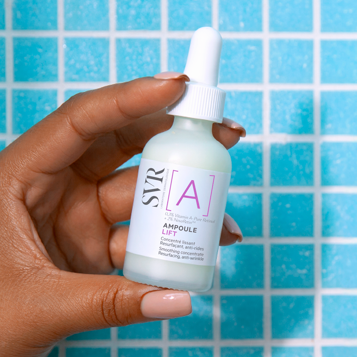 Hand holding a glass bottle of SVR Ampoule Lift retinol serum against a bright blue tiled background.