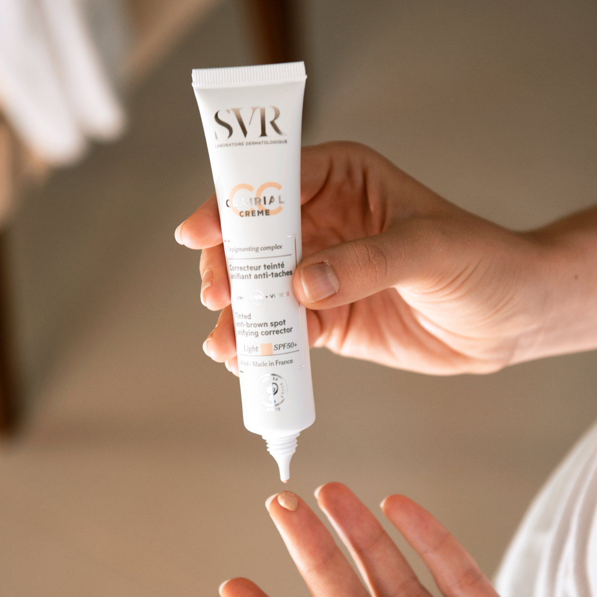 Hand holding a 40ml white tube of SVR Clairial CC Light SPF50+ cream with a drop of tinted product on a fingertip.