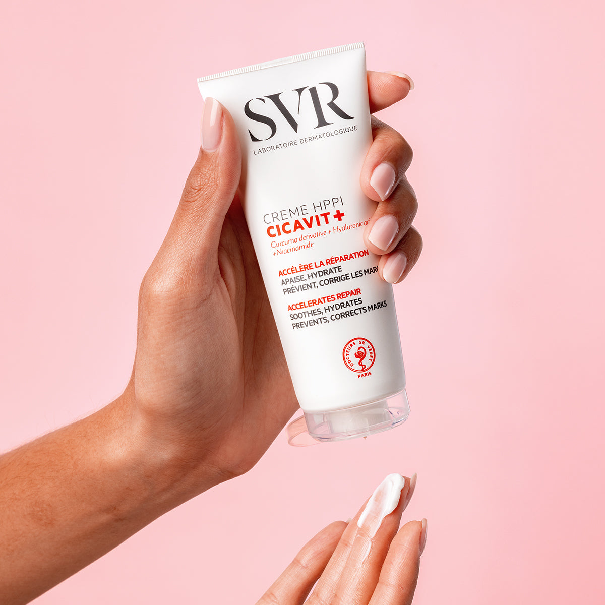 Hand holding a white SVR CICAVIT+ Crème HPPI tube with red text, dispensing a small amount of white cream onto fingertips.